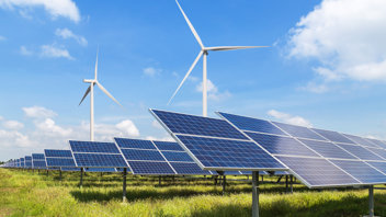Wind turbines in a field with solar panels while the sun shines